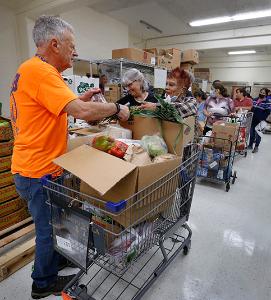 Jim Ryan, a parishioner at St. Robert Bellarmine, places a bag of organic cherries and a pineapple in a guest’s cart while Grace Digioia, a parishioner at St. Frances Borgia, grabs lettuce. (Karen Callaway/Chicago Catholic)