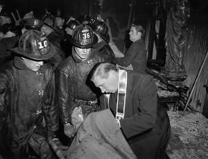 A priest blesses a fire victim while Chicago firefighters look on. (Chicago Catholic file photo)