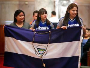 Women wearing Nicaraguan shirts and jerseys hold their home country's flag with a rosary during Mass. (Karen Callaway/Chicago Catholic)