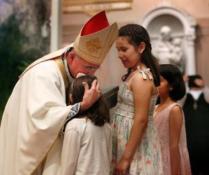 Bishop Báez kisses the head of a girl who helped bring up the gifts during Mass. (Karen Callaway/Chicago Catholic)