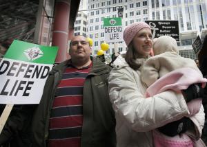 Elaine Perez, from Aurora, Illinois, holds her daughter and stands with her husband while listening to speakers at
the Thompson Center at the conclusion of the march. (Karen Callaway / Catholic New World)