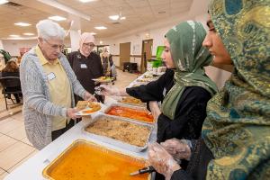Sally Nador of the Sisterhood of Salaam Shalom receives food on her plate from young Muslim women volunteers. (Deacon Randy Belice/Chicago Catholic)