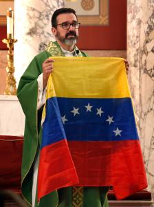 El padre Sergio Rivas sostiene la bandera de Venezuela antes de la misa.
