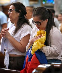 Gisela Chacón y Susan Aldana, quien sostiene la bandera de Venezuela, oran durante la misa.