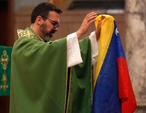 El padre Sergio Rivas dirige la oración por el pueblo venezolano mientras sostiene la bandera de ese país.