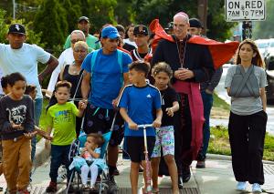 El obispo Kevin Birmingham guía a la gente por Irving Park Road para asistir a la misa en St. Pascal el 18 de junio.