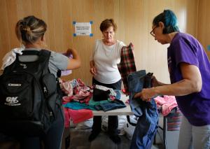 Margaret Burk y Margie McKenzie ayudan a un migrante (a la izquierda) a encontrar ropa en el albergue de emergencia en la iglesia Catherine of Siena-St. Lucy, el 8 de agosto. Fotos: Karen Callaway/Católico