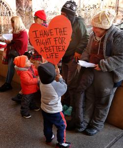 Niños con pancartas se preparan para caminar en la posada con sus familias después del rosario.